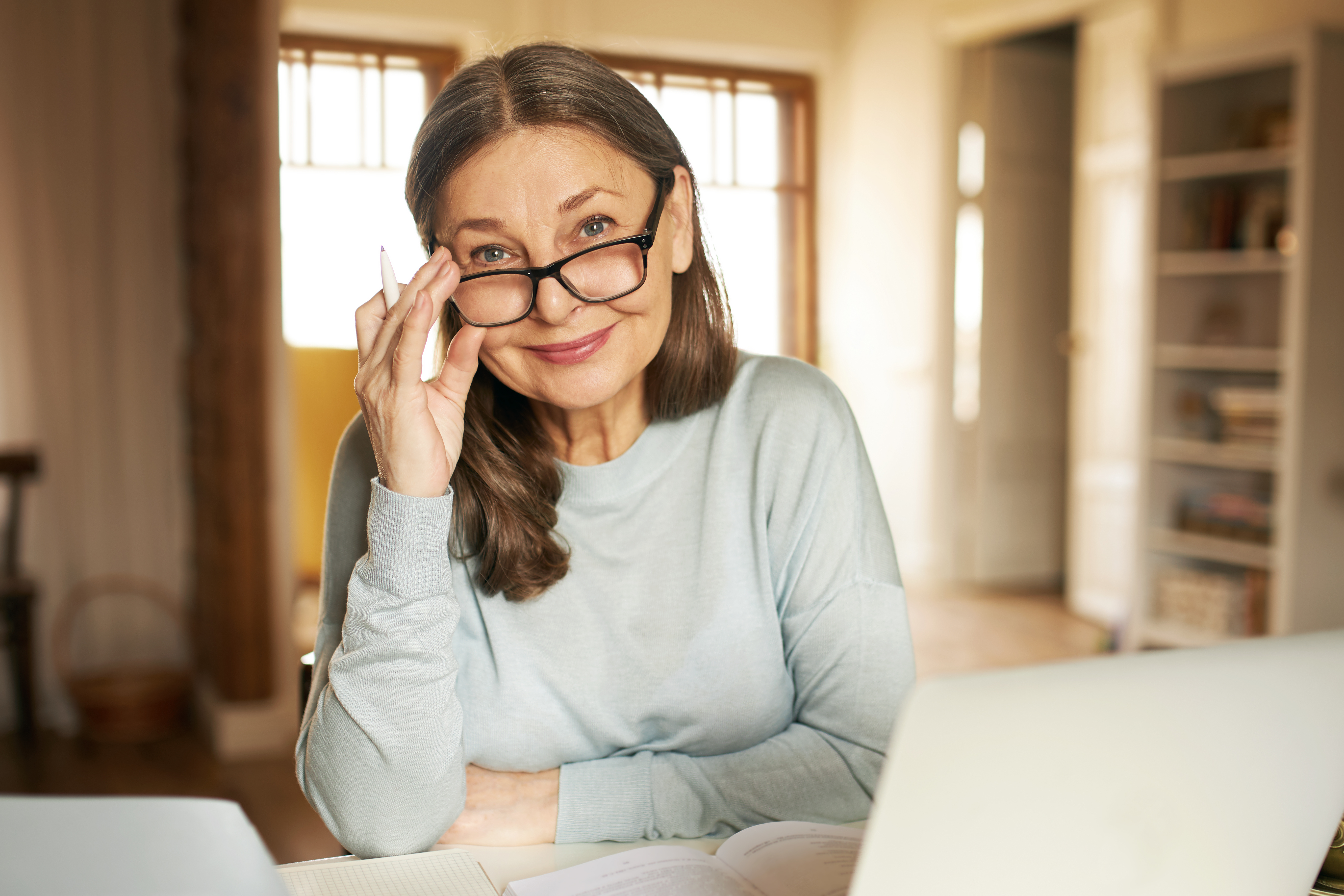 Person adjusts glasses while sitting at a home desk and working on a laptop.